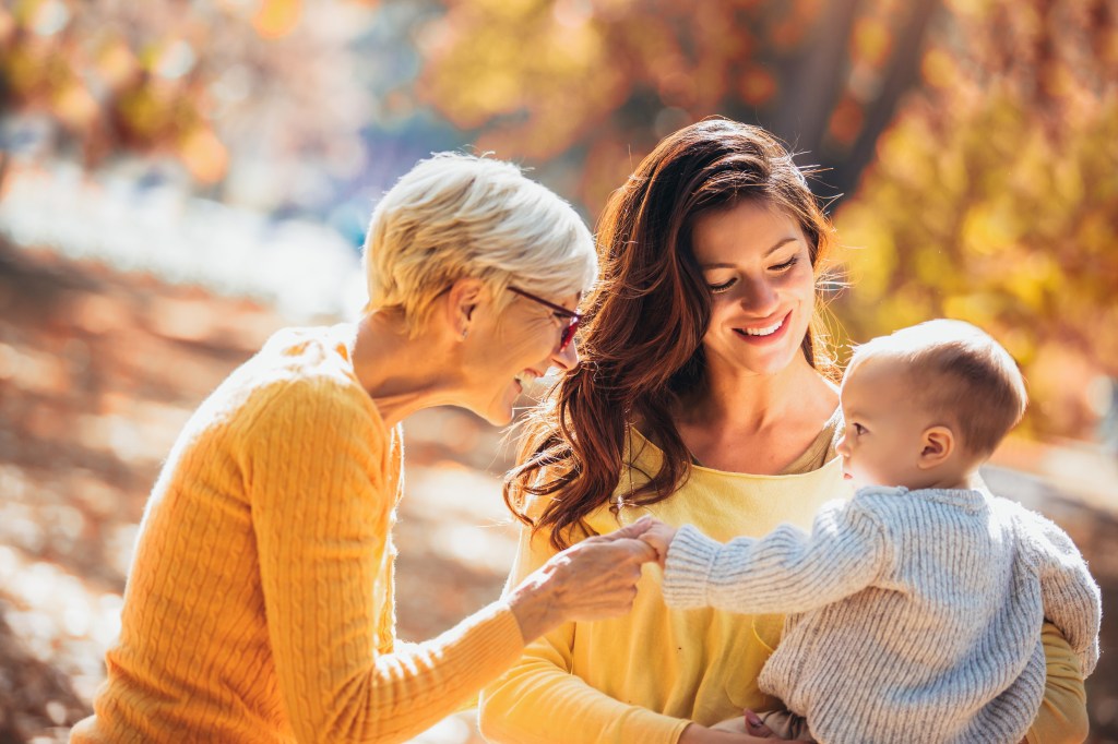 Grandmother and mother smiling at baby in an autumn park